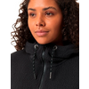 Nahaufnahme eines jungen Frauengesichts mit lockigem Haar, sie trägt einen schwarzen Pullover mit hohem Kragen und Kordelzug