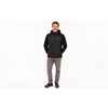 Man in a black quilted jacket with hood, gray pants and black shoes, standing against a white background, hands in pockets, smiling