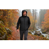 A man wearing a black hooded jacket with hands in his pockets walks on a forest path covered with autumn leaves beside a stream