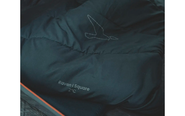 Zusammengerollter dunkelblauer Schlafsack mit orangem Rand auf dunklem Untergrund