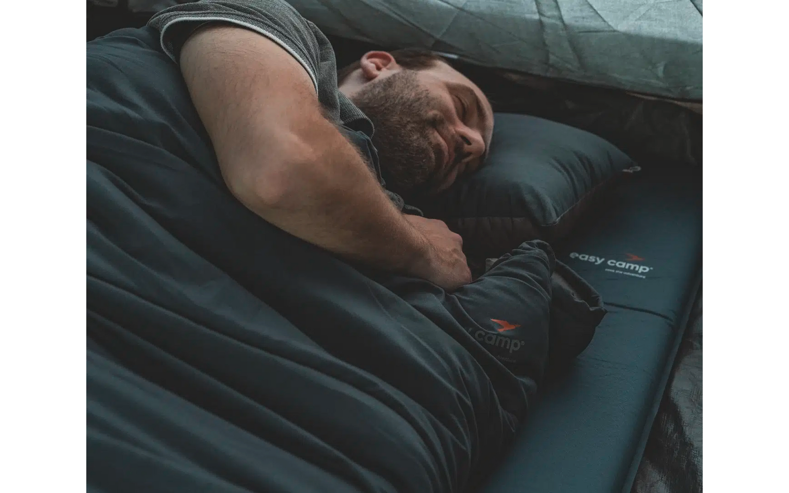 Mann liegt schlafend auf einer Luftmatratze unter einer Decke