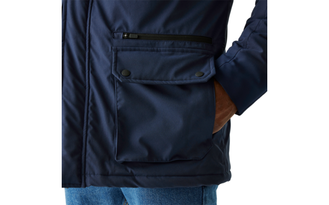 Person trägt eine dunkle Jacke mit aufgesetzter Tasche und hat eine Hand in der Hosentasche