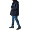 Ein Mann trägt eine blaue Winterjacke, blaue Jeans und schwarze Schuhe, er blickt zur Seite und steht vor einem hellen Hintergrund