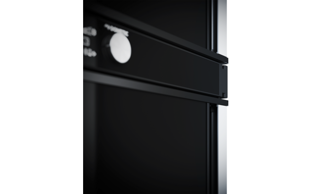 Nahaufnahme eines schwarzen Geräts mit horizontalem Griff, rundem weißen Knopf und glänzender Oberfläche; rechts ein vertikaler Lichtreflex