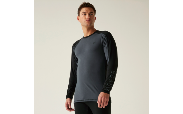 Mann in langärmligem Shirt mit dunkelgrauem Rumpf und schwarzen Ärmeln, sichtbares Logo auf der Brust, Schriftzug auf einem Ärmel, schwarze Hose, steht vor hellem Hintergrund und blickt leicht nach oben und zur Seite