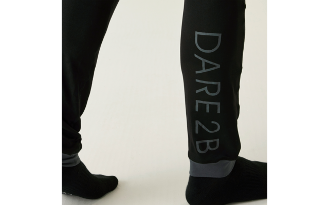 Untere Beine in schwarzen Jogginghosen, Hosenbein mit senkrechter Aufschrift "DARE2B", schwarze Socken, heller Hintergrund