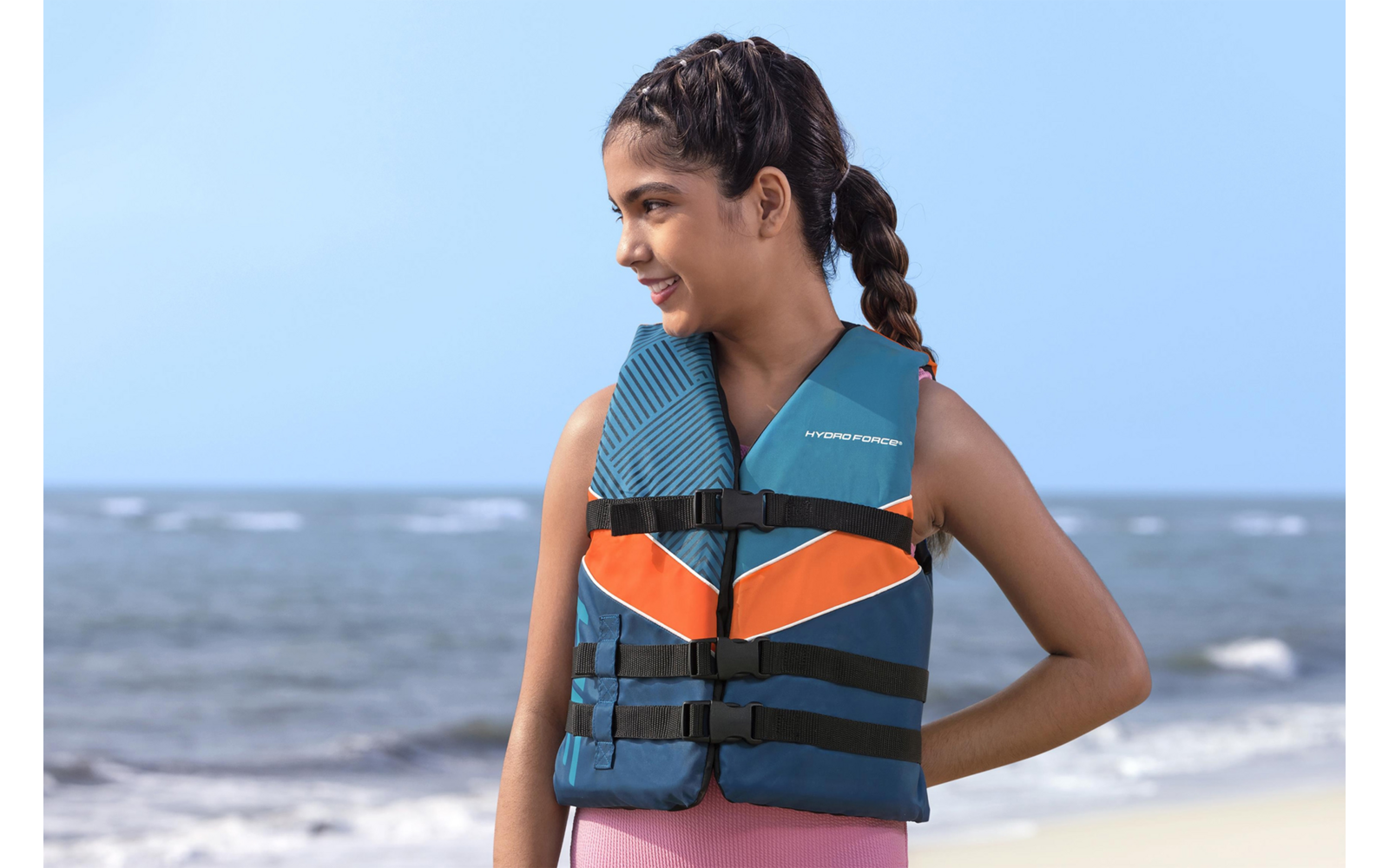 Mädchen am Strand mit einer blau-orangefarbenen Rettungsweste, schaut nach rechts