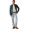 Staande persoon met donkerblauw geruit overshirt over een wit T‑shirt, lichtblauwe spijkerbroek, bruine riem, bruine veterschoenen, horloge om linkerpols