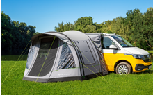 Yellow car with gray tent on green grass and trees in the background
