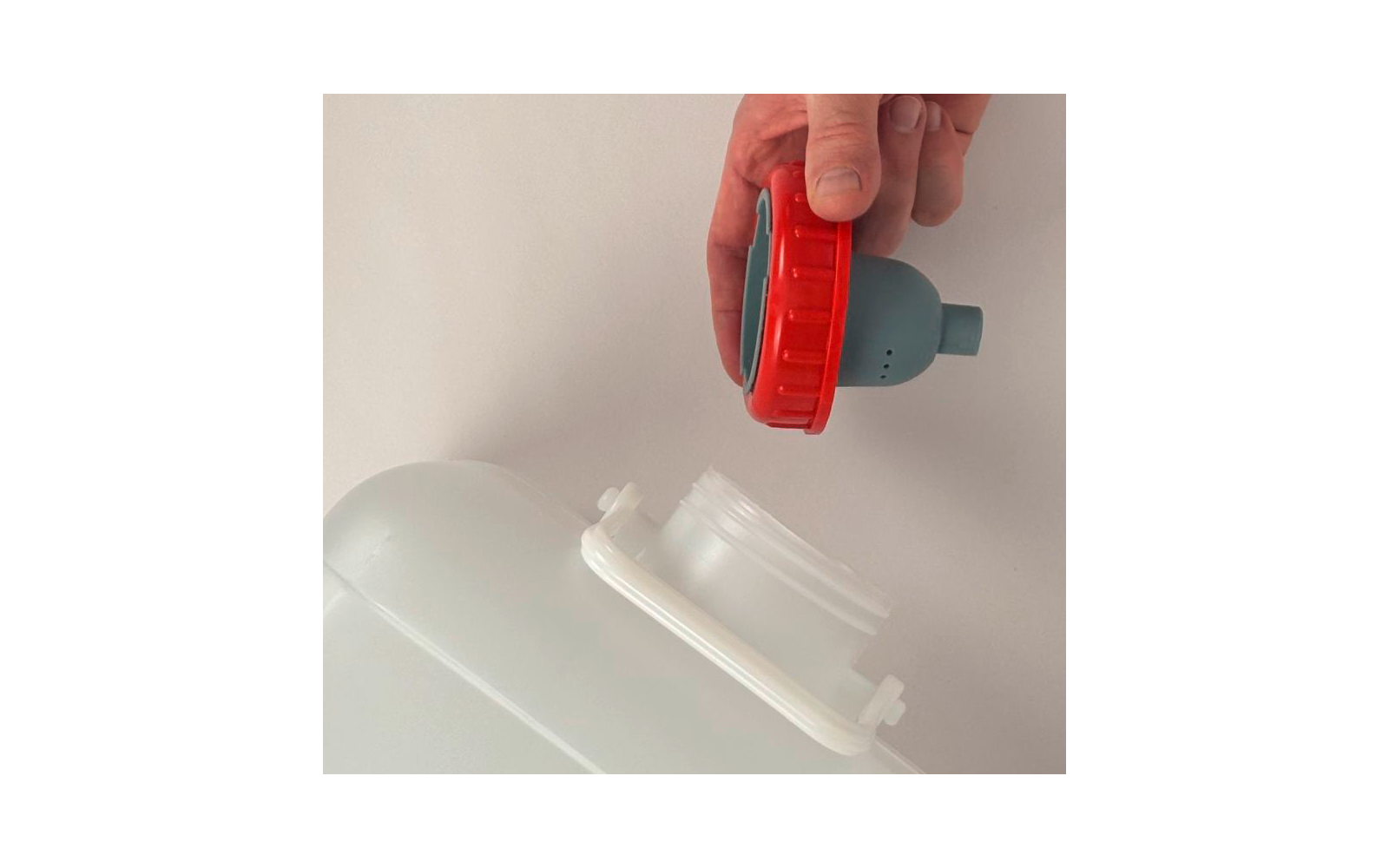 Hand hält roten Deckel mit grüner Innenfläche über offenem weißen Plastikkanister