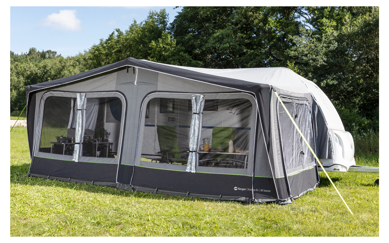 Large gray awning with white windows on green grass, surrounded by trees