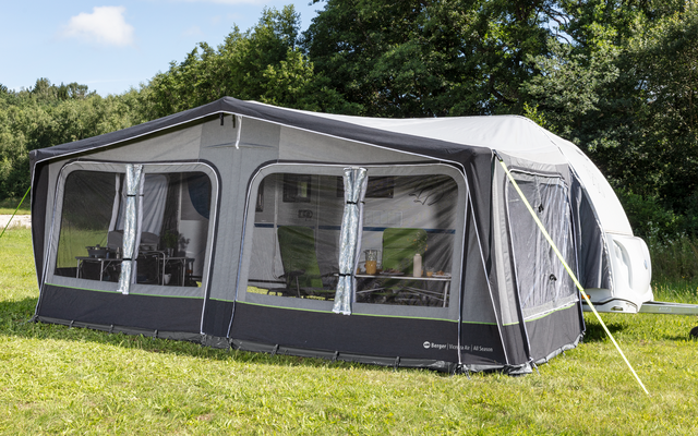 Large gray awning with white windows on green grass, surrounded by trees