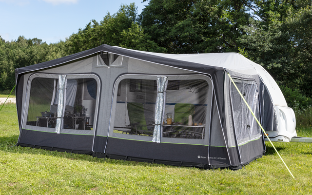 A large gray caravan awning stands on a grassy area with trees in the background