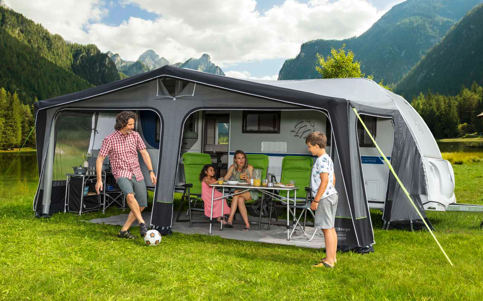 Family with two children in front of a motorhome on a green meadow with mountains in the background