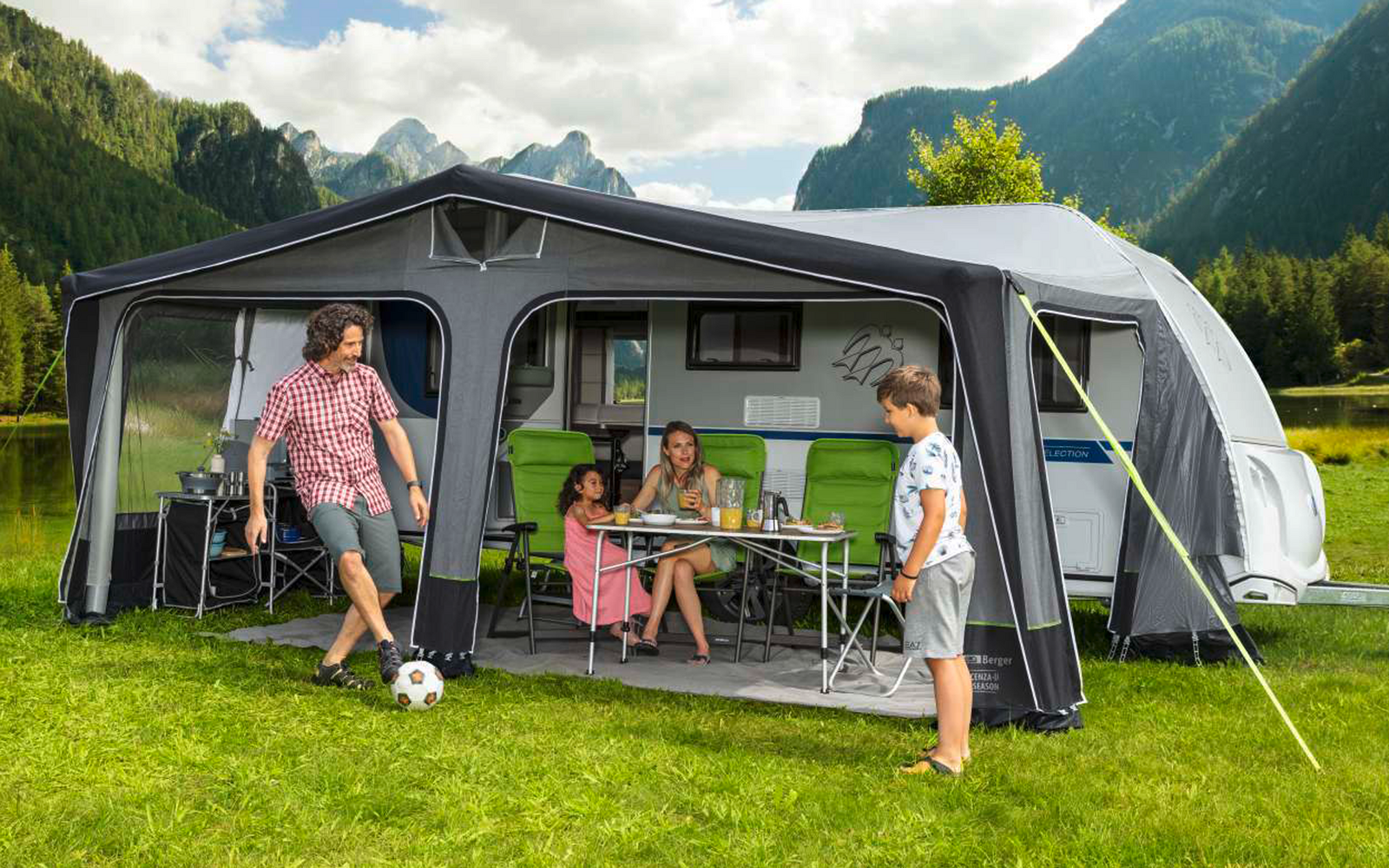 Family in front of a camper with an awning tent on a green meadow in the mountains