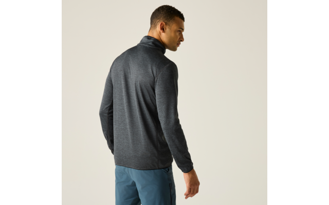 Mann steht mit dem Rücken zur Kamera, Kopf nach links gedreht, trägt grauen Pullover mit Stehkragen und blaue Hose vor hellem einfarbigem Hintergrund