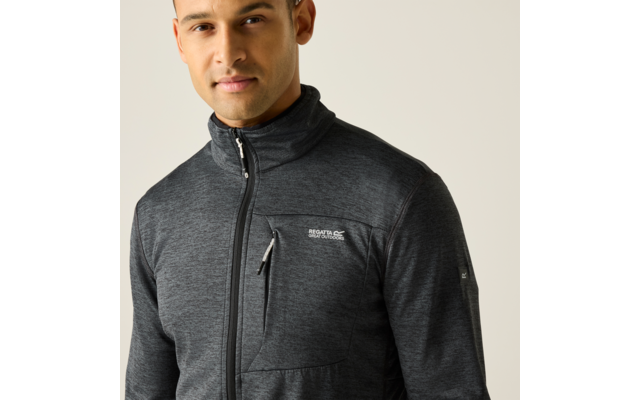 Mann, Brust aufwärts, heller Hintergrund, dunkelgraue Zip-Jacke mit Reißverschlusstasche und kleinem Logo auf linker Brust, leichtes Lächeln