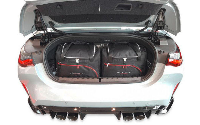 Geöffneter Kofferraum eines weißen Autos mit zwei schwarzen Reisetaschen mit roten Details; vier Auspuffendrohre unter der Stoßstange sichtbar