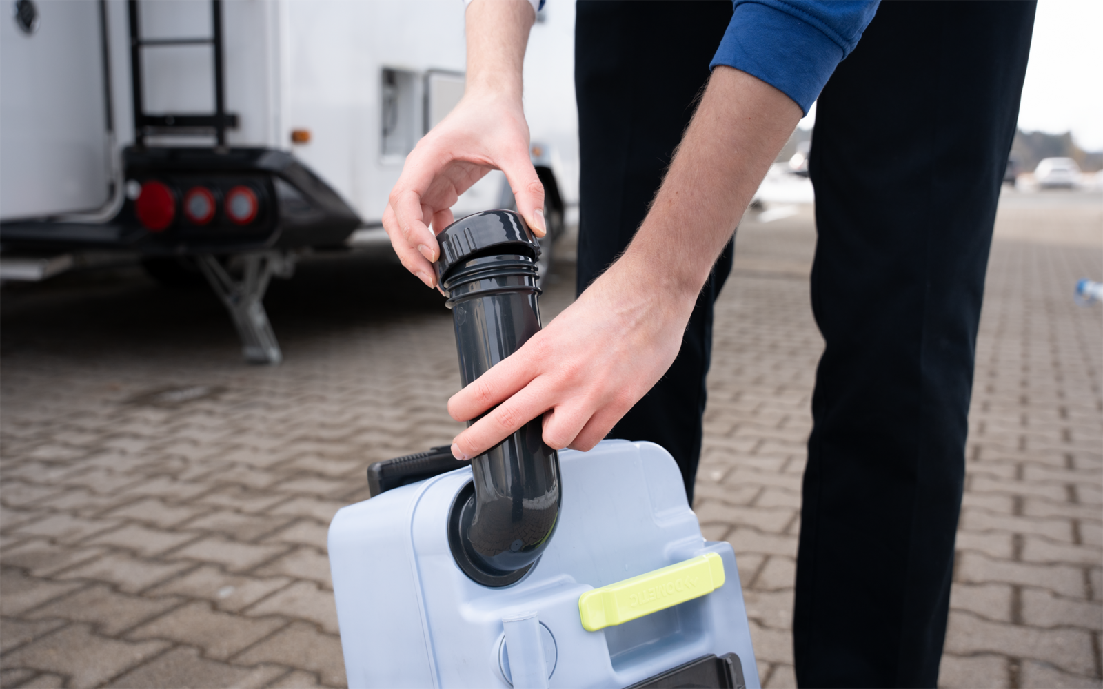 Person führt schwarzen Auslass in weißen Plastikbehälter neben einem Wohnwagen auf gepflastertem Untergrund ein