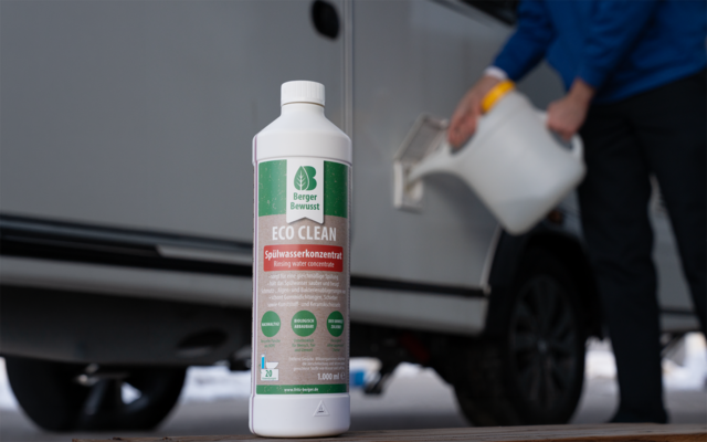 Weiße Flasche mit grünem Etikett 'Eco Clean' im Vordergrund; im Hintergrund gießt eine Person aus einem weißen Kanister in einen Einfüllstutzen eines weißen Fahrzeugs