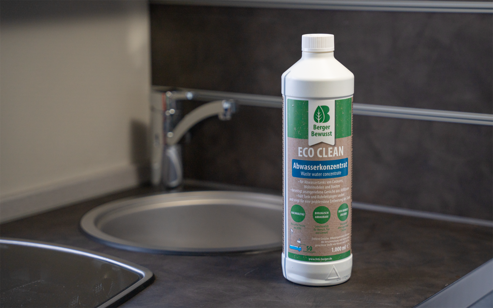 Weiße Kunststoffflasche mit grünem Etikett 'ECO CLEAN Abflusskonzentrat' steht auf dunkler Arbeitsfläche neben rundem Spülbecken und verchromtem Wasserhahn vor dunkler Flieswand