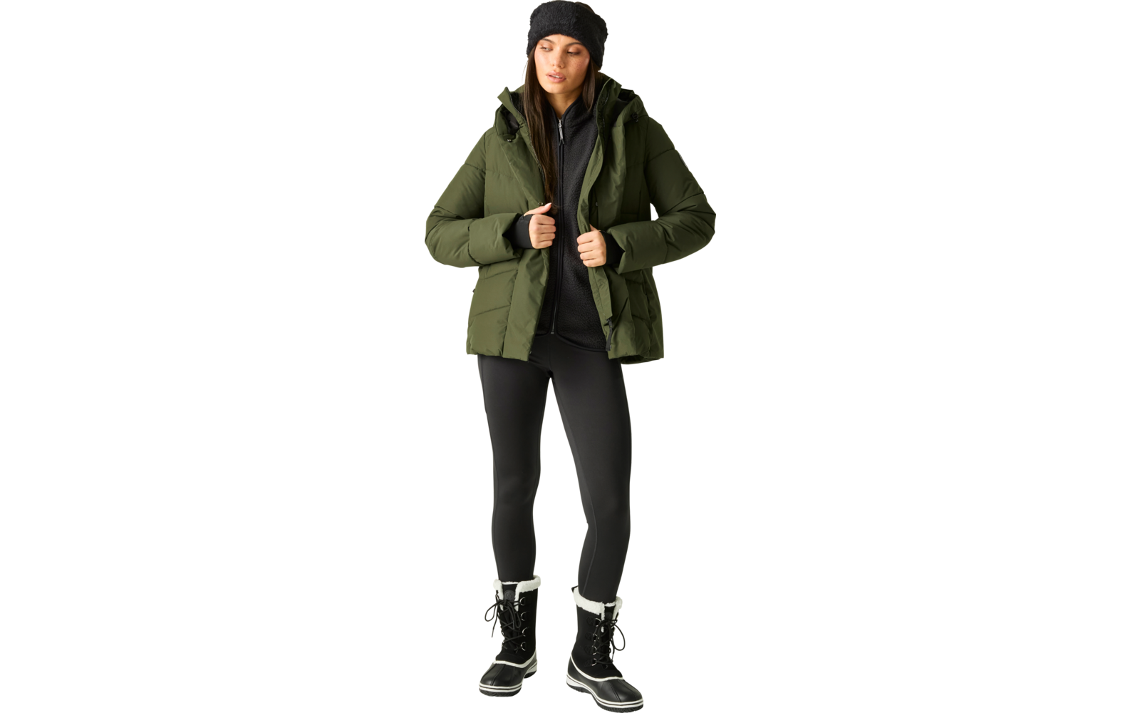 Person steht, trägt grüne gesteppte Winterjacke mit Kapuze, schwarze Strickmütze, schwarzen Reißverschluss-Pullover, schwarze Leggings und schwarze Winterstiefel mit weißem Fellbesatz; Hände halten die Jackenkanten