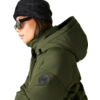 Person im Profil mit dunkelgrauer Strickmütze, schwarzer Sonnenbrille und olivgrüner Steppjacke mit Kapuze und rundem Ärmelpatch