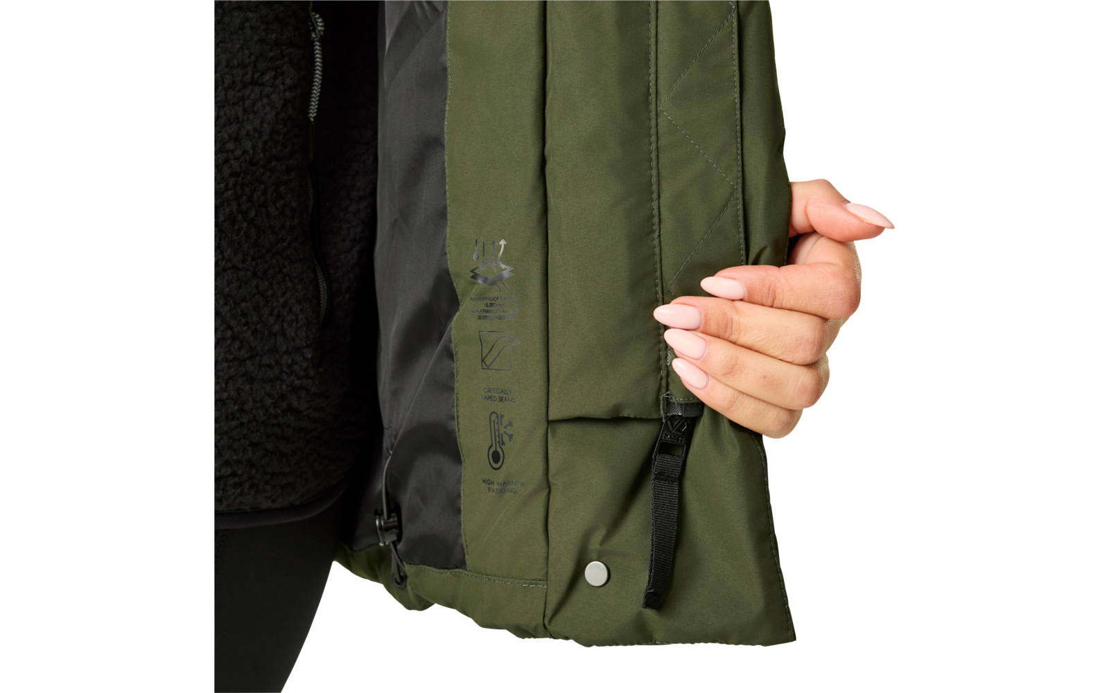 Hand mit hellrosa lackierten Fingernägeln hält den Saum einer olivgrünen Jacke; sichtbares schwarzes Innenfutter, Reißverschluss, Druckknopf, schwarze Zugschlaufe und bedruckte Symbole auf dem Stoff
