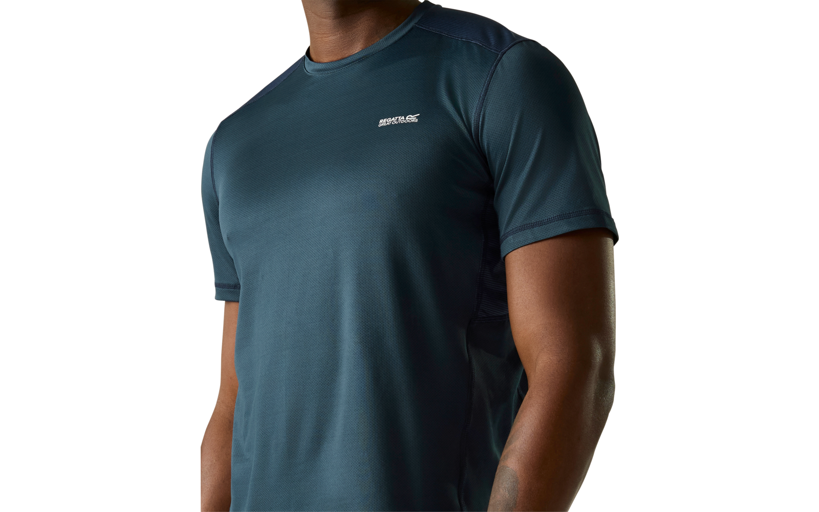 Oberkörper einer Person in kurzärmeligem dunkelgrün-blauem Sportshirt mit rundem Halsausschnitt und kleinem weißen Logo auf der linken Brust; Tattoo am linken Unterarm sichtbar