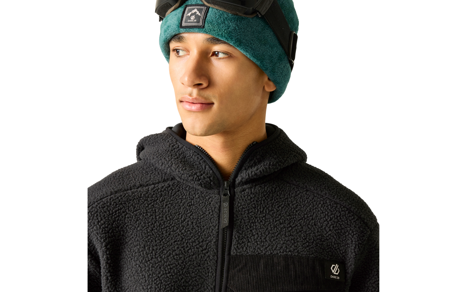 Person mit grüner Mütze und Skibrille auf der Stirn, blickt nach links, trägt eine schwarze Fleecejacke mit Reißverschluss und kleinem Logo