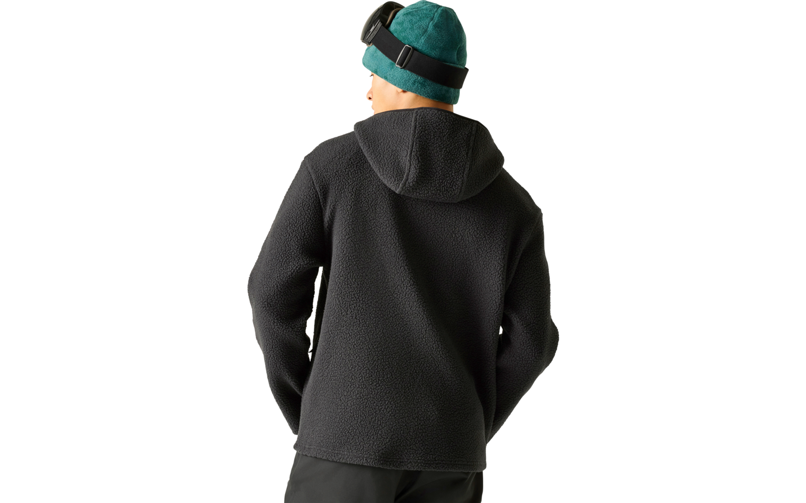 Person von hinten, dunkelgraue Kapuzen-Fleecejacke, türkisgrüne Strickmütze mit schwarzem Brillenband, dunkle Hose, heller Hintergrund