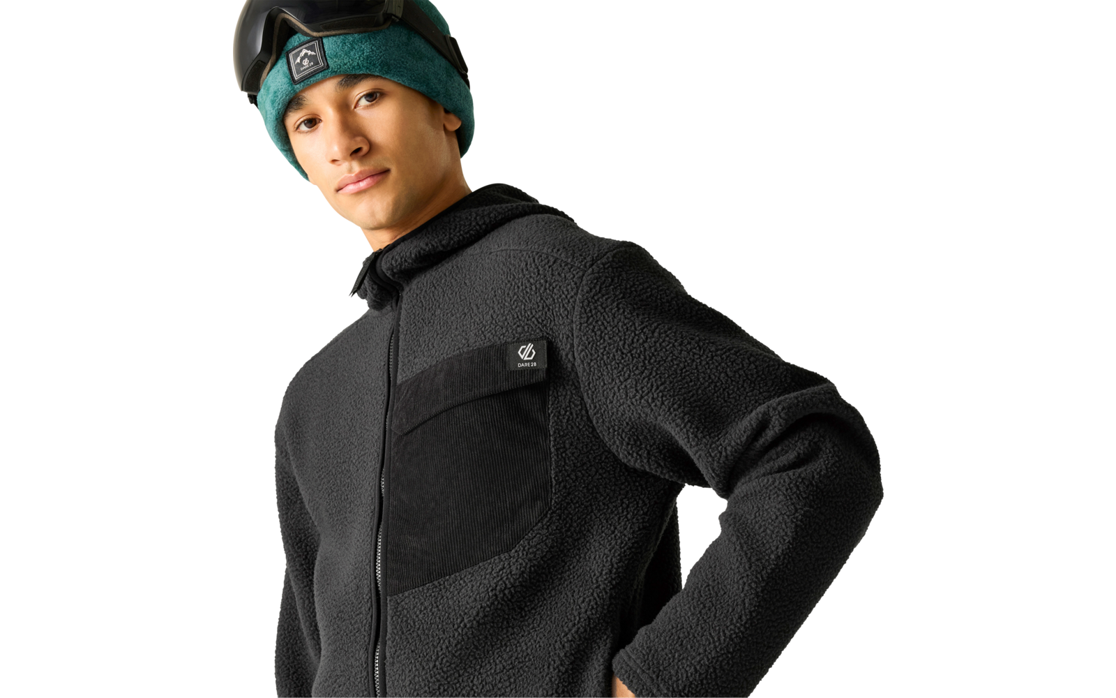 Person mit dunkler Fleecejacke, grüner Mütze und Skibrille auf der Stirn vor hellem Hintergrund