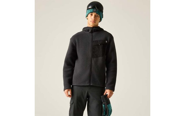 Person vor hellem Hintergrund, trägt schwarze Fleecejacke mit Brusttasche und Reißverschluss, schwarze Hose, türkise Mütze unter schwarzem Helm und hält türkise-schwarze Handschuhe