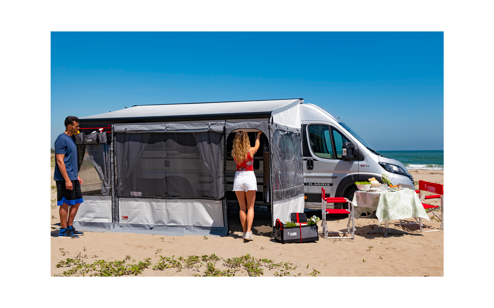 Camping-car sur la plage avec auvent déployé, deux personnes et équipement de camping