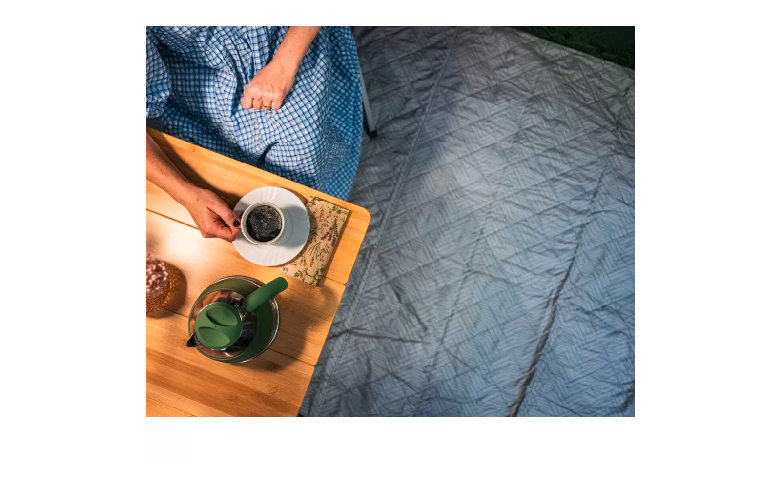 Holztablett mit grünem Teekännchen und weißer Tasse auf grauem Bett