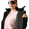 Person mit schwarzer Sonnenbrille, rosa Fleecejacke und schwarzem Wintermantel, hält den Jackenkragen