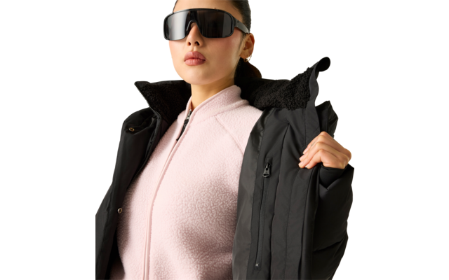 Person mit schwarzer Sonnenbrille, rosa Fleecejacke und schwarzem Wintermantel, hält den Jackenkragen