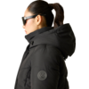 Person im Profil mit schwarzer Sonnenbrille, schwarzer gesteppter Jacke mit Kapuze, Pferdeschwanz und kleinem Ohrring
