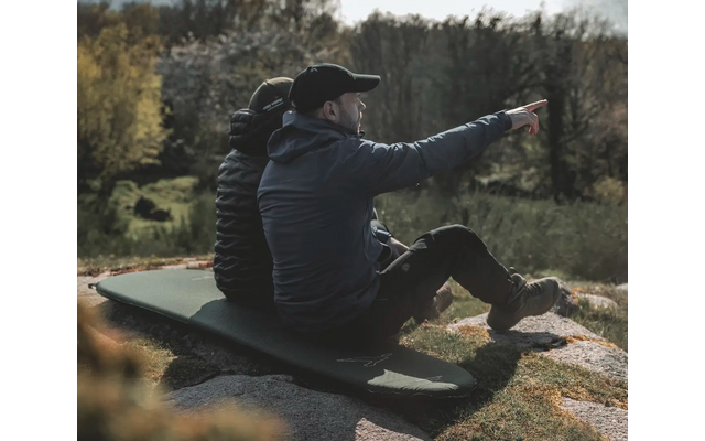 Zwei Männer sitzen auf einem Baumstamm im Wald, einer zeigt in die Ferne
