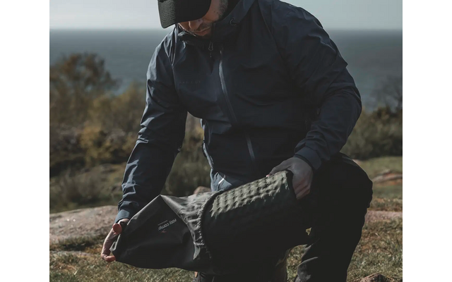 Person in dunkler Outdoor-Bekleidung kniet auf dem Boden und zieht einen schwarzen Schuh an