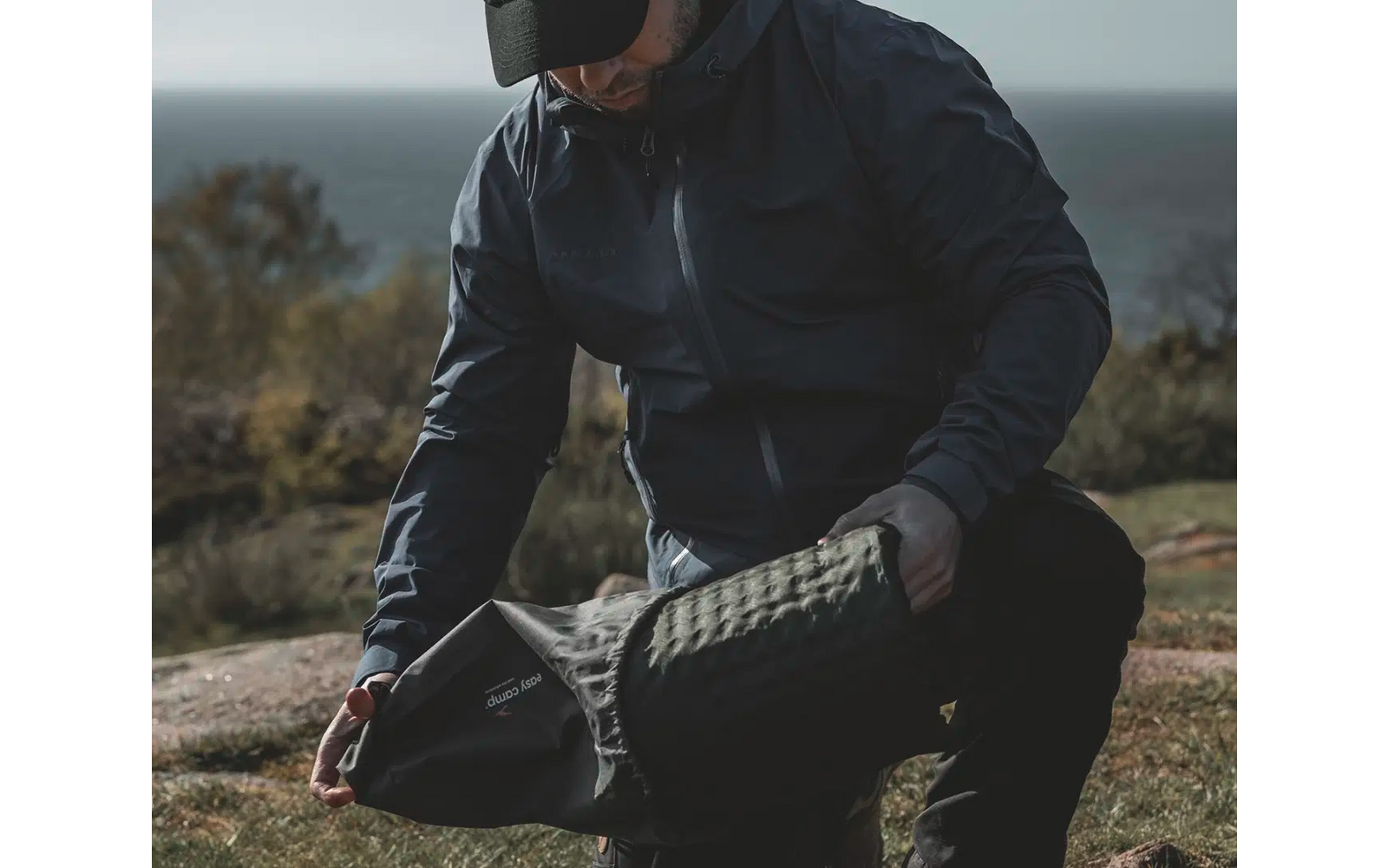 Person in dunkler Outdoor-Bekleidung kniet auf dem Boden und zieht einen schwarzen Schuh an