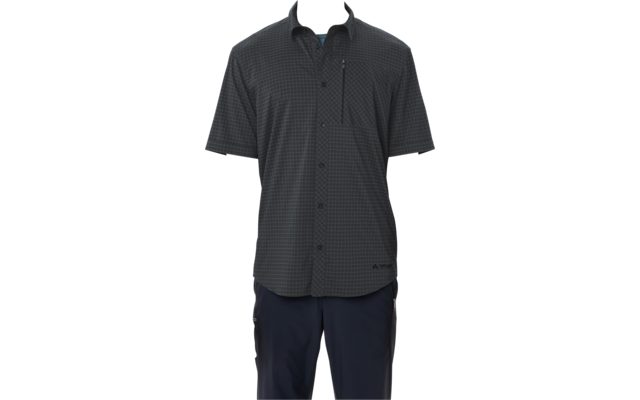 Persona con cabello corto y oscuro de pie sobre fondo blanco, viste una camisa de manga corta oscura con cuadros pequeños, abotonada y con bolsillo con cremallera en el pecho, y pantalones oscuros