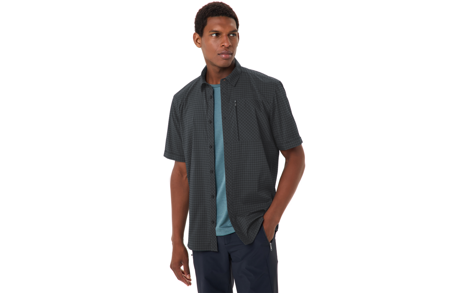 Person trägt dunkel kariertes kurzärmeliges Hemd über türkisfarbenem T-Shirt, Hände in den Taschen, schaut zur Seite vor weißem Hintergrund