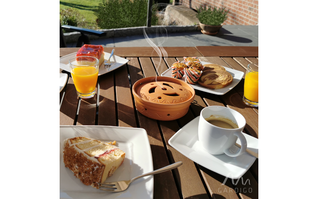 Tisch mit Frühstück im Freien, auf dem verschiedene Getränke, Kaffee und Gebäck stehen