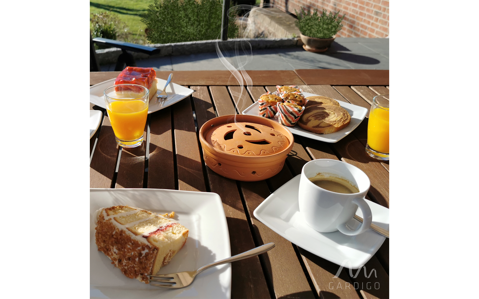 Tisch mit Frühstück im Freien, auf dem verschiedene Getränke, Kaffee und Gebäck stehen