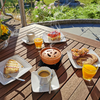 Holztisch mit mehreren Tellern, einer Kaffeetasse, einem Glas Orangensaft und einer Teekanne im Freien
