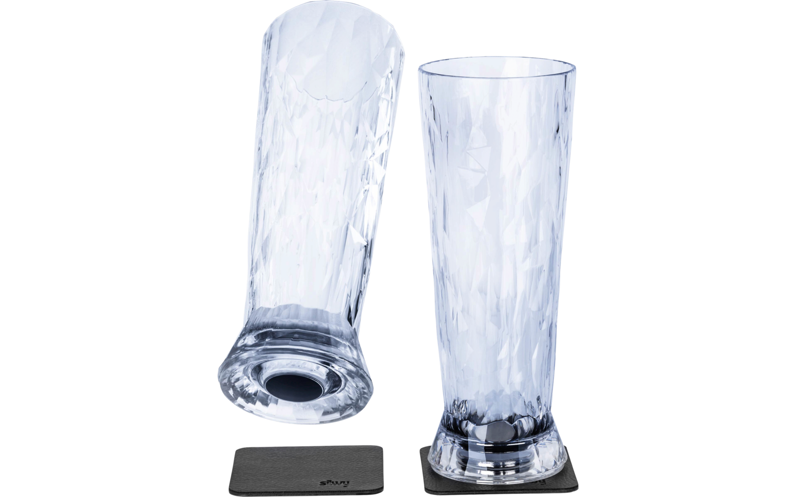 Two transparent textured glasses, one standing on a black coaster, one lying down