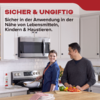 Man en vrouw in moderne keuken, man snijdt groenten, vrouw staat glimlachend bij het fornuis