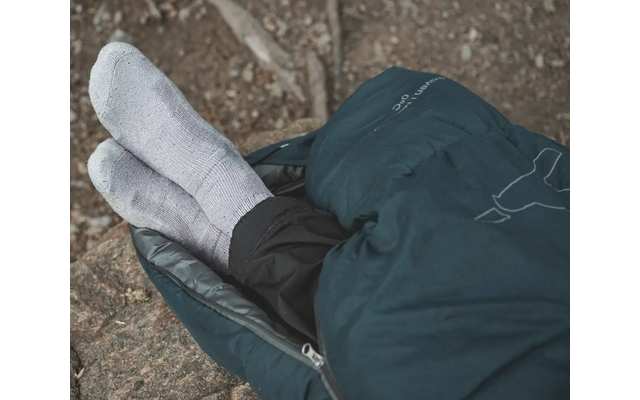 Zwei weiße Schuhe auf einem steinigen Boden neben einer blauen Jacke