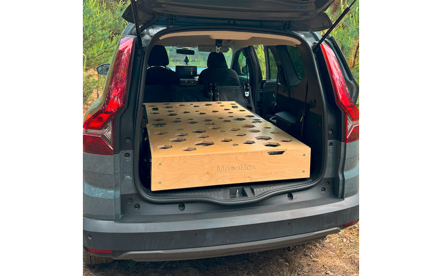 Offener Kofferraum eines grauen SUVs, darin eine große flache Holzbox mit mehreren runden und sternförmigen Ausschnitten; Seitenfläche mit Schriftzug „MoonBox“